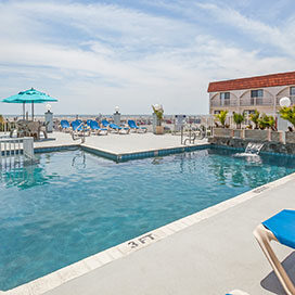 Outdoor pool with lounge chairs and ocean view at Days Inn and Suites Wildwood